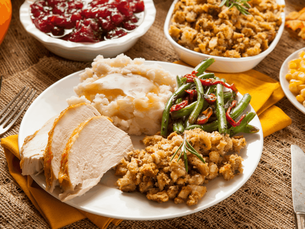 Plate with turkey, mashed potatoes, green beans, and stuffing, surrounded by additional dishes on a table.